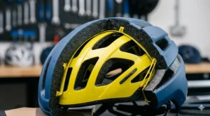 Close-up technical shot of a sectioned blue cycle helmet revealing the internal bright yellow MIPS low-friction slip-plane layer attached to the black EPS foam shell.