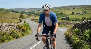 Road cyclist ascending a steep hill in the British countryside wearing an unzipped jersey and summer cycling base layer.