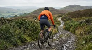Gravel cyclist wearing a breathable packable cycling jacket on a muddy trail in the Peak District.