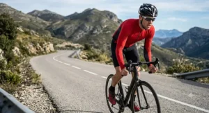 Male cyclist climbing a steep hill wearing a red men's breathable long sleeve cycling jersey with moisture-wicking fabric panels.