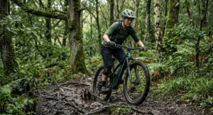 A mountain biker tackling a muddy trail track wearing a relaxed-fit women's cycling jersey in olive green.