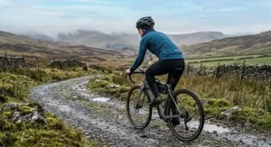 A cyclist on a gravel trail wearing a windproof and waterproof women's cycling jersey for unpredictable British weather.