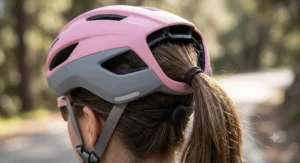 A women's road cycling helmet in pink and grey, showing the rear retention system designed to accommodate a high ponytail.