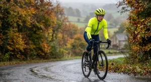 Woman cyclist in a high-visibility yellow women's waterproof long sleeve cycling jersey riding through autumn drizzle.